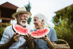 Cheerful older adults having fun while eating watermelon in the backyard.