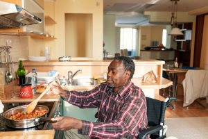 Older adult, who uses a wheelchair, cooking at the kitchen stove.