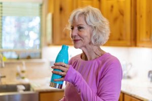 An older adult drinking water from a reusable bottle.
